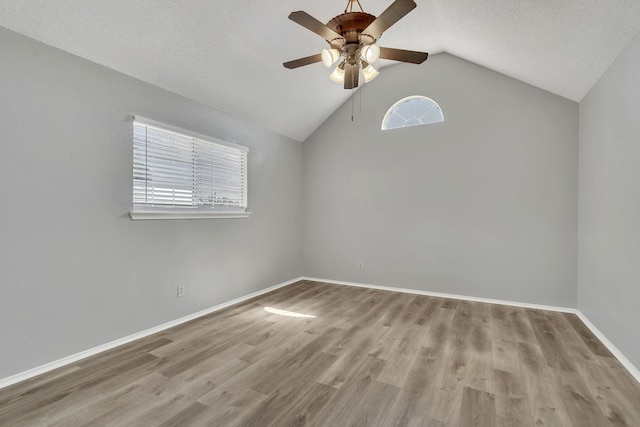 spare room with a textured ceiling, light hardwood / wood-style floors, vaulted ceiling, and ceiling fan