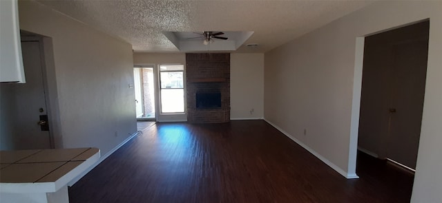 unfurnished living room with a textured ceiling, dark hardwood / wood-style flooring, ceiling fan, and a brick fireplace