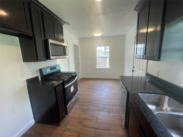 kitchen with sink, a textured ceiling, stainless steel appliances, dark hardwood / wood-style floors, and dark stone counters