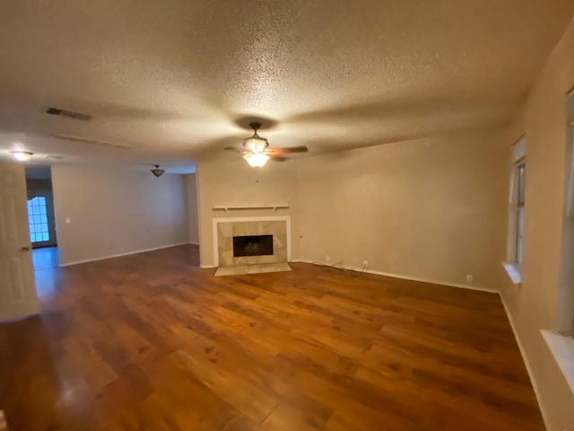 unfurnished living room featuring wood-type flooring, a tiled fireplace, ceiling fan, and a textured ceiling