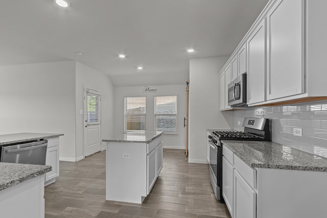 kitchen featuring white cabinets, a center island, appliances with stainless steel finishes, and light stone counters