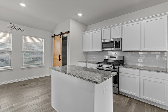 kitchen featuring appliances with stainless steel finishes, white cabinets, a barn door, light stone countertops, and light wood-type flooring