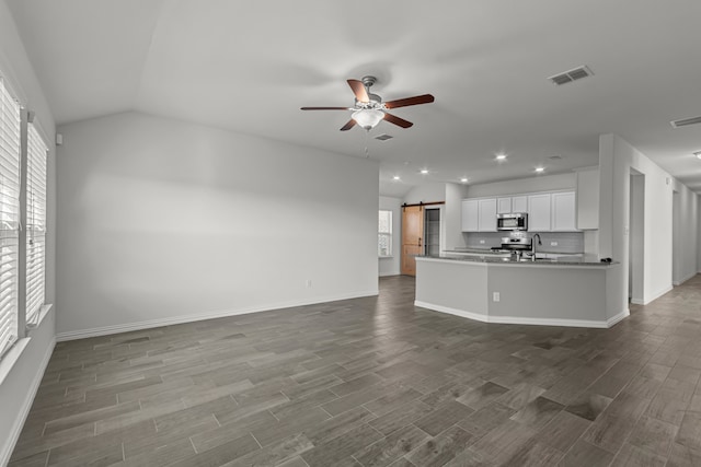 unfurnished living room featuring ceiling fan, lofted ceiling, sink, hardwood / wood-style floors, and a barn door