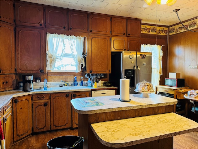 kitchen featuring light hardwood / wood-style floors, a center island, sink, wood walls, and stainless steel refrigerator with ice dispenser