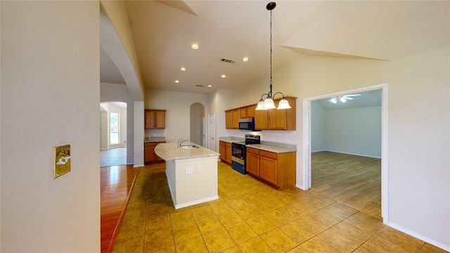 kitchen with appliances with stainless steel finishes, hanging light fixtures, light hardwood / wood-style floors, ceiling fan with notable chandelier, and a center island with sink