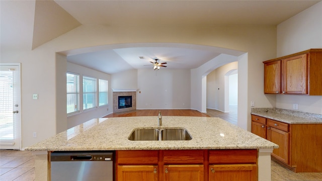 kitchen featuring a kitchen island with sink, sink, a tiled fireplace, ceiling fan, and stainless steel dishwasher