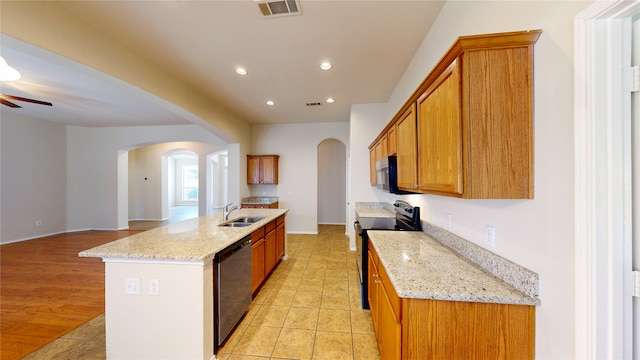 kitchen with sink, an island with sink, black appliances, light stone countertops, and ceiling fan