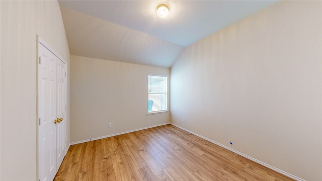 spare room featuring light wood-type flooring and vaulted ceiling