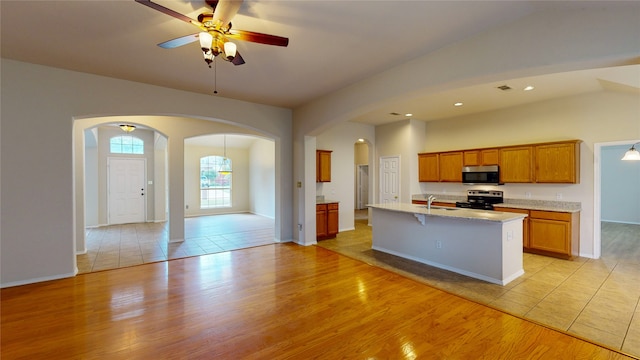 kitchen with light hardwood / wood-style floors, a kitchen island with sink, sink, stainless steel appliances, and ceiling fan