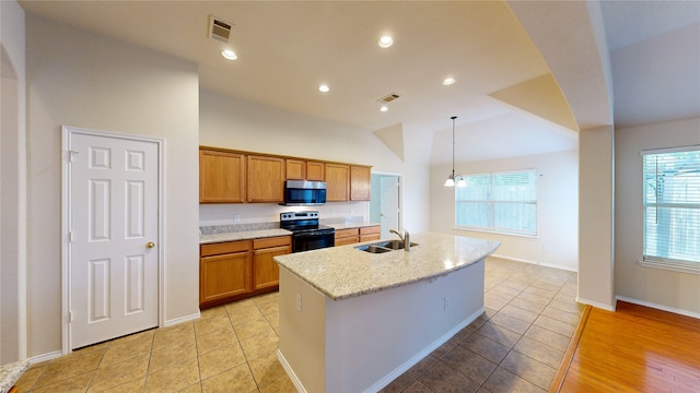 kitchen featuring light stone countertops, pendant lighting, stainless steel appliances, lofted ceiling, and a center island with sink