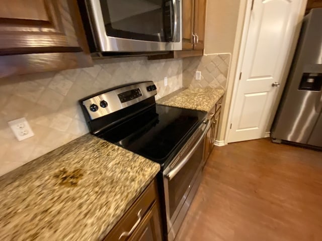 kitchen featuring light stone counters, appliances with stainless steel finishes, dark wood-type flooring, and tasteful backsplash