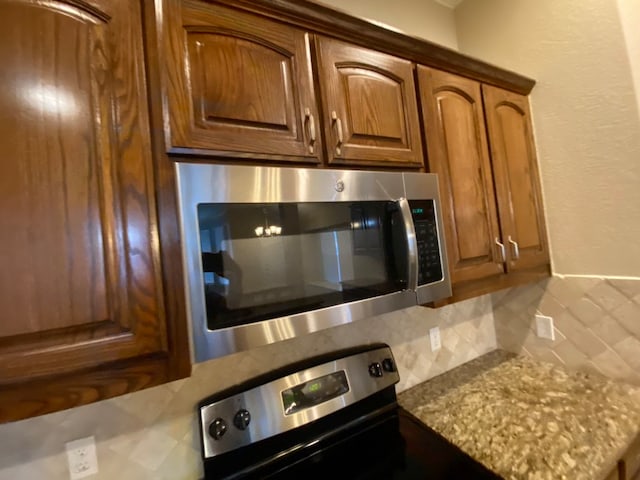 interior details with light stone counters, appliances with stainless steel finishes, and backsplash