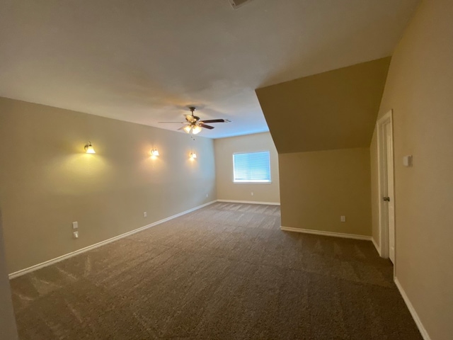 additional living space with lofted ceiling, dark colored carpet, and ceiling fan