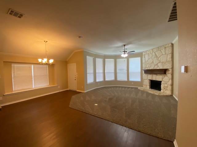 unfurnished living room featuring a stone fireplace, dark wood-type flooring, ceiling fan with notable chandelier, crown molding, and vaulted ceiling