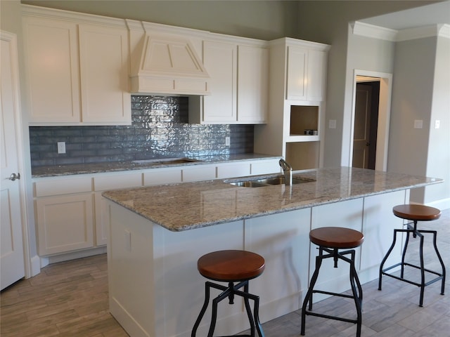 kitchen with an island with sink, white cabinets, light hardwood / wood-style flooring, premium range hood, and sink