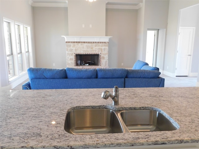 kitchen with a stone fireplace, ornamental molding, and sink