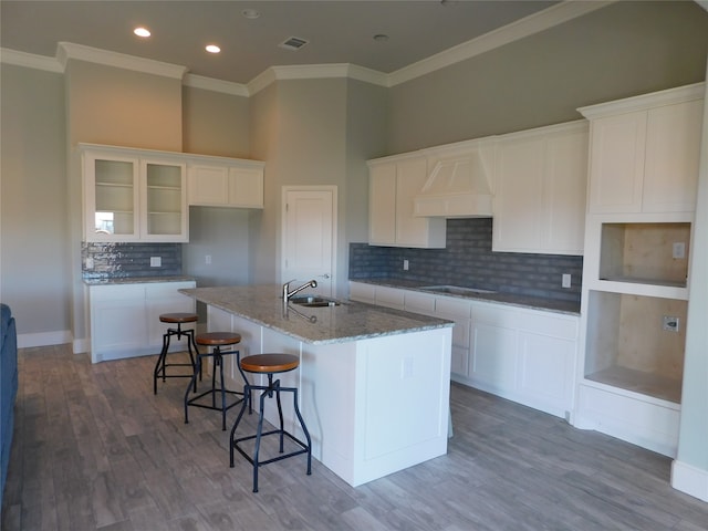 kitchen with white cabinets, hardwood / wood-style flooring, a kitchen island with sink, and premium range hood