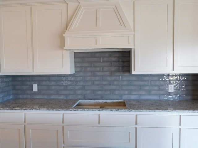 kitchen with light stone countertops, white cabinetry, tasteful backsplash, and custom exhaust hood