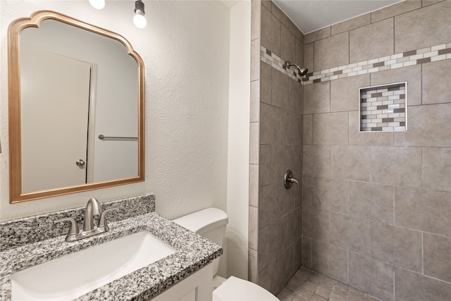 bathroom with tiled shower, vanity, and toilet