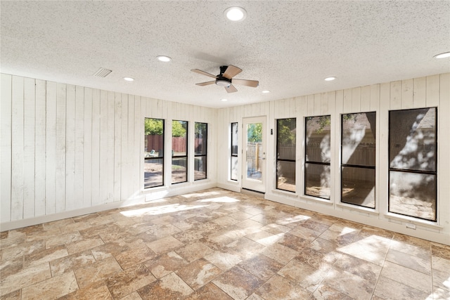 empty room with wood walls, ceiling fan, and a textured ceiling