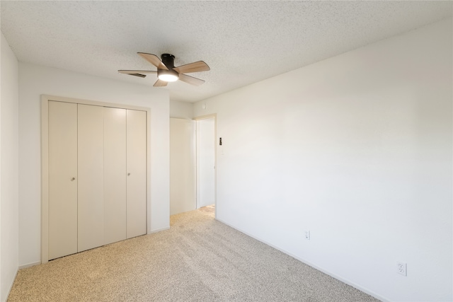 unfurnished bedroom featuring a textured ceiling, ceiling fan, light colored carpet, and a closet