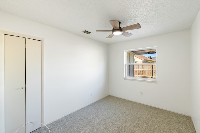 unfurnished bedroom with a textured ceiling, carpet flooring, ceiling fan, and a closet