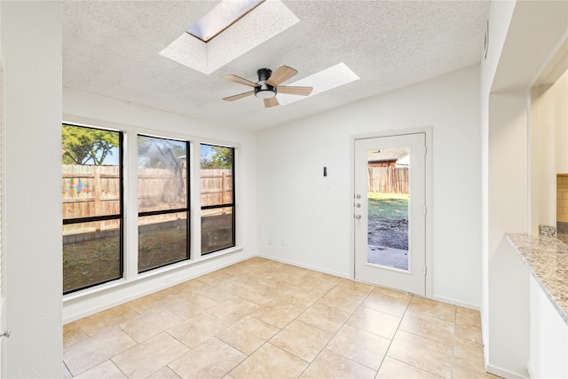 unfurnished dining area featuring ceiling fan, a textured ceiling, vaulted ceiling with skylight, and light tile patterned flooring