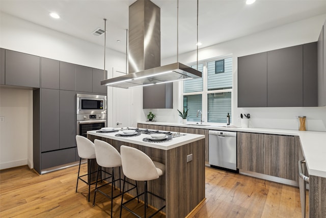 kitchen with light wood-type flooring, a center island, island exhaust hood, a kitchen bar, and appliances with stainless steel finishes