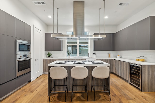 kitchen featuring light wood-type flooring, beverage cooler, a kitchen island, stainless steel appliances, and decorative light fixtures