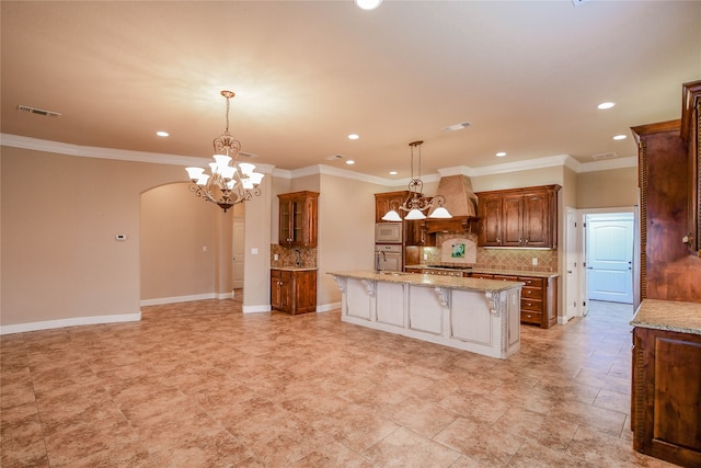 kitchen featuring a breakfast bar area, an island with sink, hanging light fixtures, backsplash, and crown molding