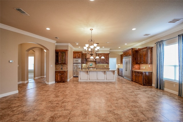 kitchen featuring pendant lighting, an island with sink, ornamental molding, backsplash, and built in appliances