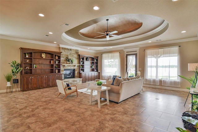 tiled living room with crown molding, a fireplace, a tray ceiling, and ceiling fan