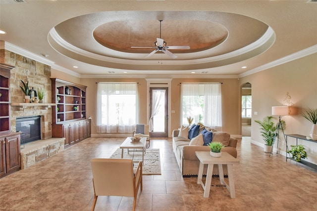 living room with a tray ceiling, a healthy amount of sunlight, and a stone fireplace