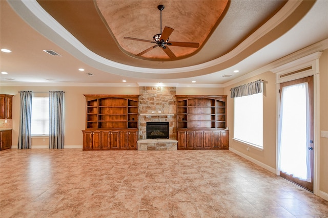 unfurnished living room with a stone fireplace, a tray ceiling, and plenty of natural light