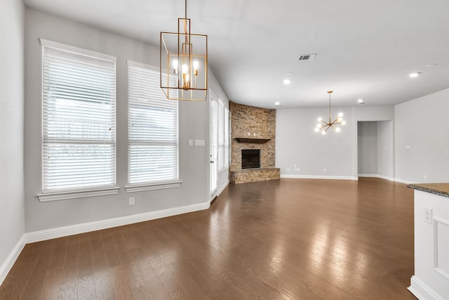 unfurnished living room with a stone fireplace, dark hardwood / wood-style floors, and a chandelier