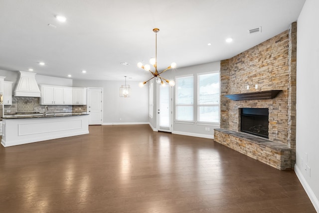 unfurnished living room with a stone fireplace, dark wood-type flooring, a chandelier, and sink