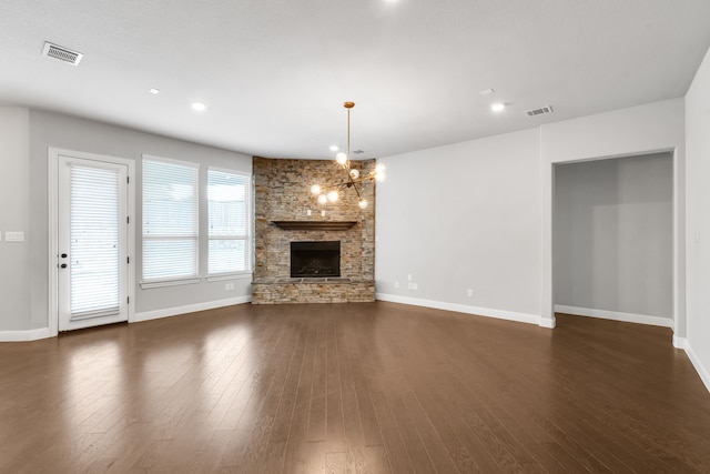 unfurnished living room with a stone fireplace, an inviting chandelier, and dark wood-type flooring