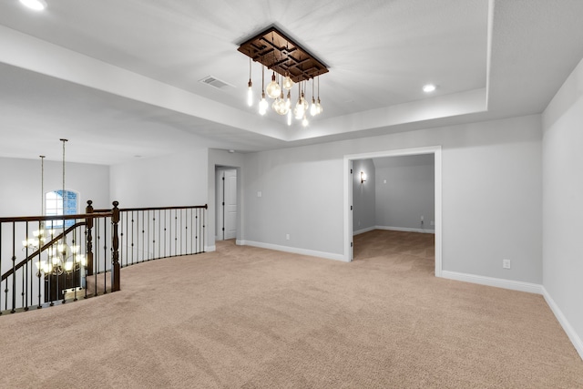 unfurnished room featuring a raised ceiling, a chandelier, and light colored carpet