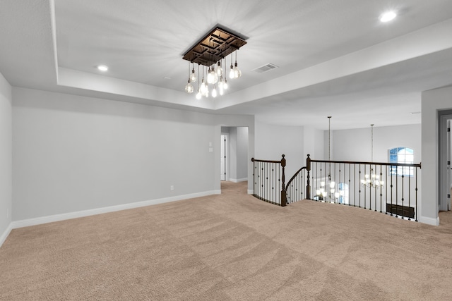 spare room featuring light colored carpet, a notable chandelier, and a raised ceiling