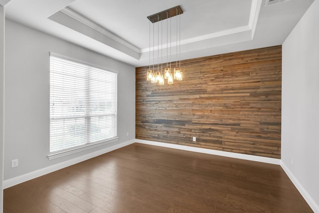 empty room featuring an inviting chandelier, wood walls, a raised ceiling, and dark hardwood / wood-style floors