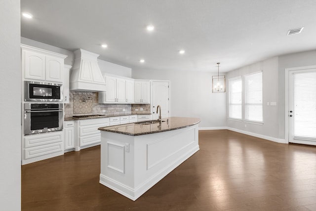 kitchen featuring stainless steel appliances, white cabinetry, a center island with sink, and custom exhaust hood