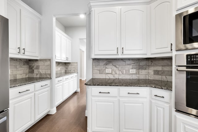 kitchen with dark stone counters, dark hardwood / wood-style floors, tasteful backsplash, white cabinetry, and appliances with stainless steel finishes