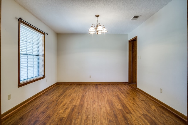 empty room with an inviting chandelier, a textured ceiling, and hardwood / wood-style floors