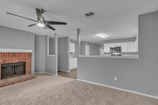 unfurnished living room with ceiling fan, light colored carpet, a textured ceiling, and a fireplace