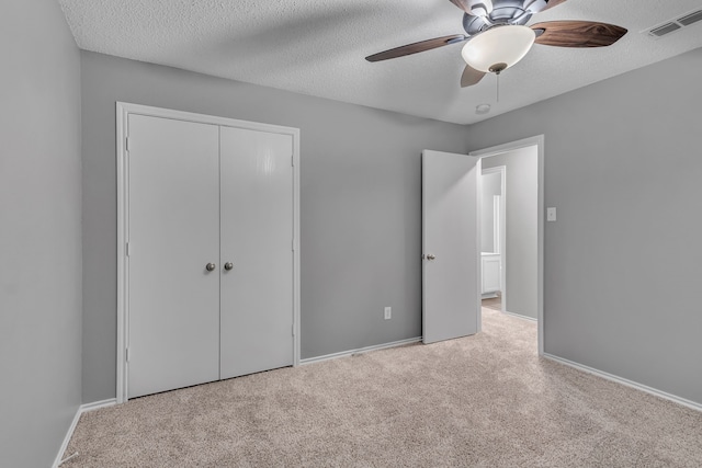 unfurnished bedroom with a closet, ceiling fan, light colored carpet, and a textured ceiling