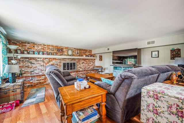 living room featuring light wood-type flooring, brick wall, and a brick fireplace