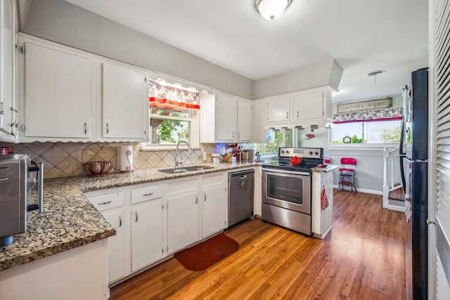 kitchen featuring light stone counters, white cabinets, stainless steel appliances, light wood-type flooring, and sink