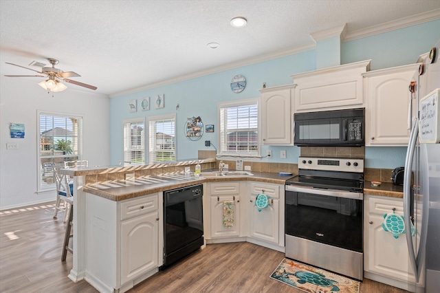 kitchen featuring a healthy amount of sunlight, black appliances, kitchen peninsula, and white cabinetry