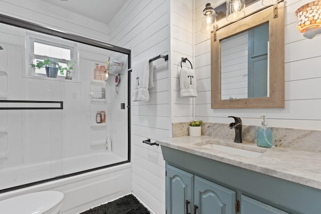 full bathroom with wood walls, combined bath / shower with glass door, vanity, and toilet