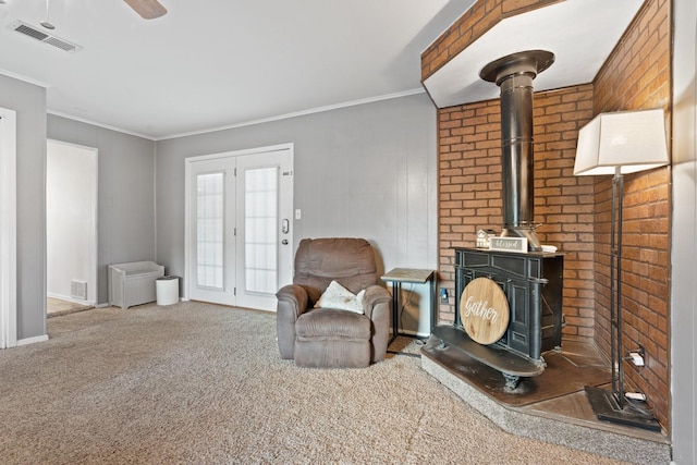 living area with a wood stove, carpet floors, ornamental molding, ceiling fan, and french doors